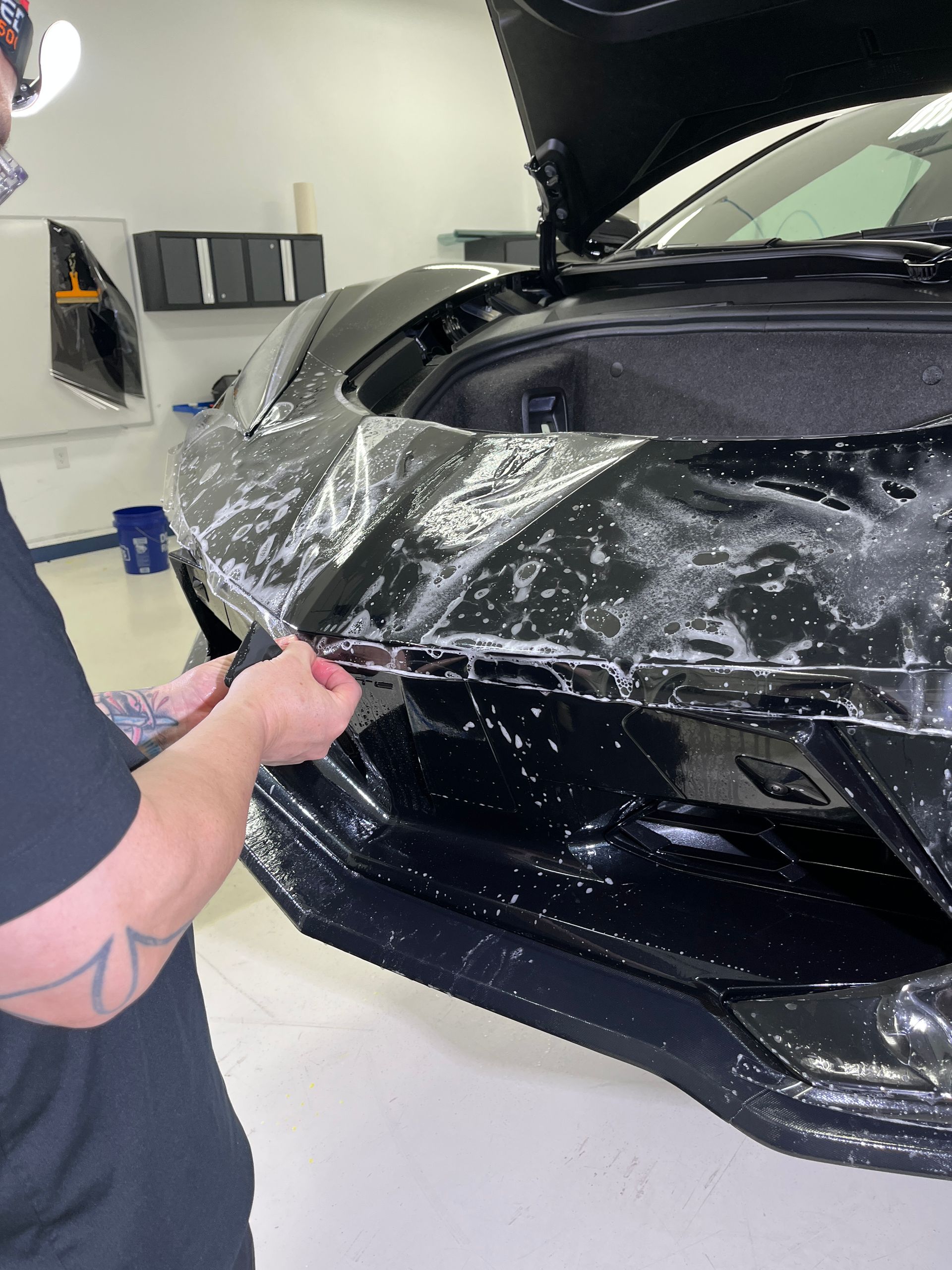 XPEL paint protection film being installed on the front of a black Corvette Stingray