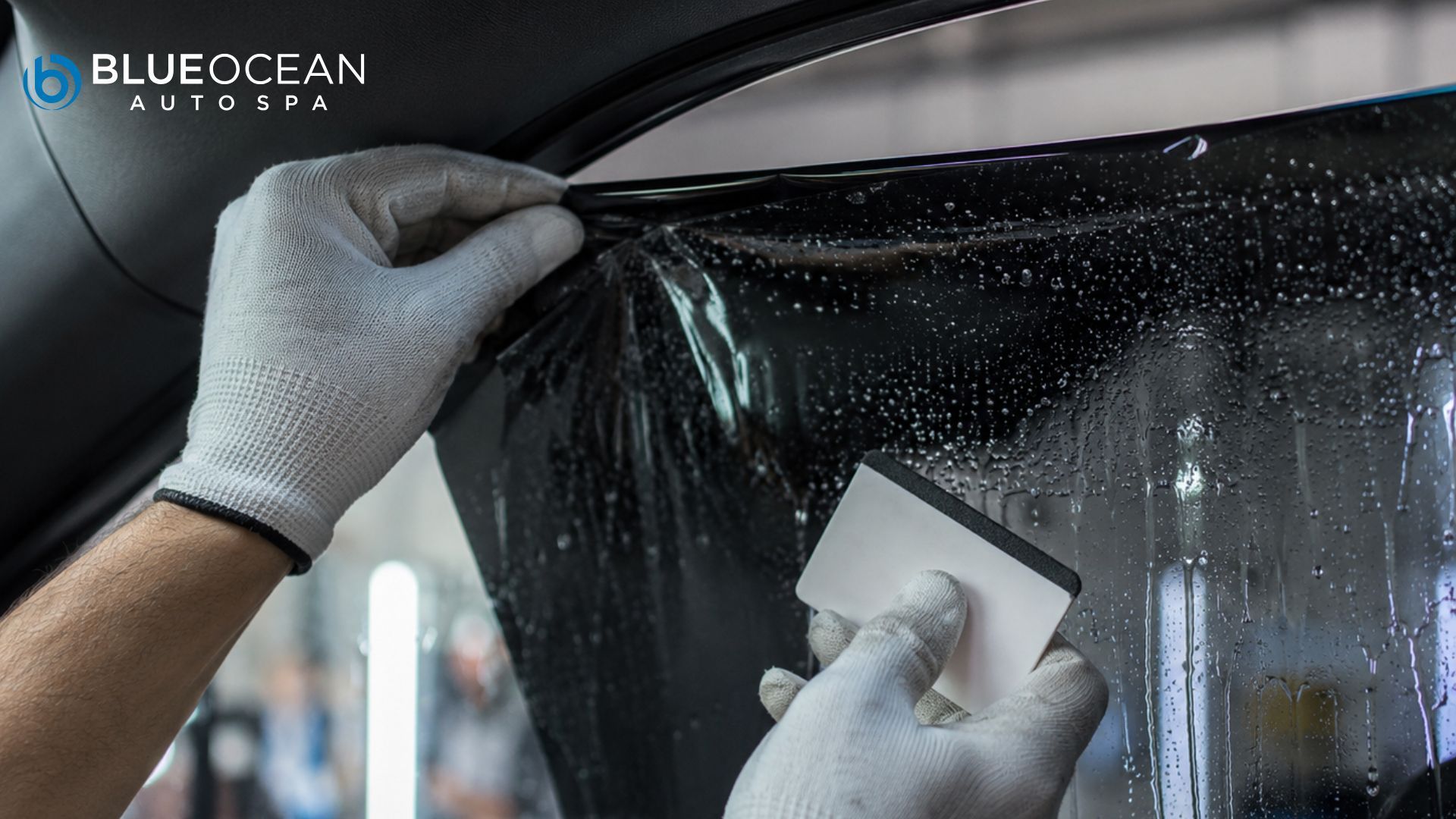 A technician uses a squeegee to apply window tint to a wet car door window. The text