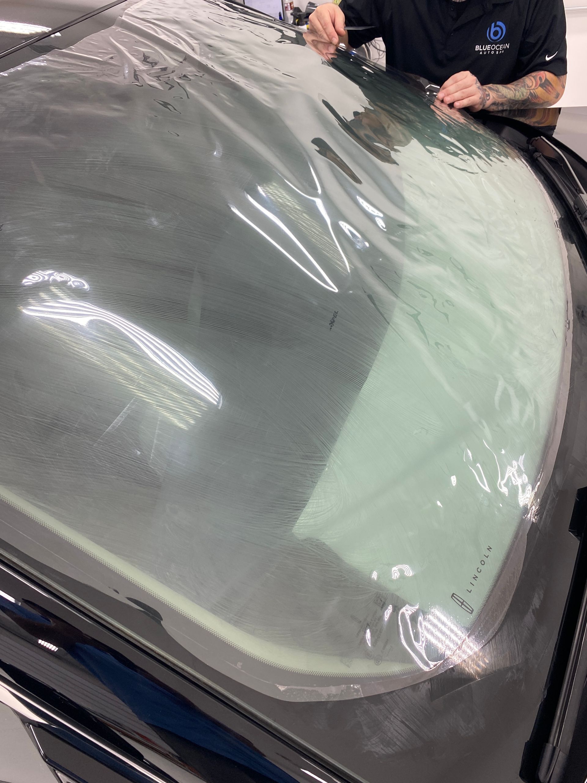 A man is covering the windshield of a car with plastic.