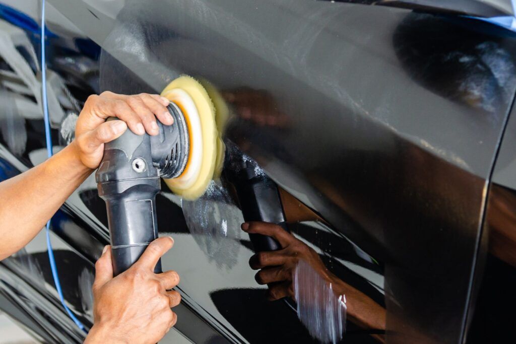 A person is polishing a black car with a polisher.