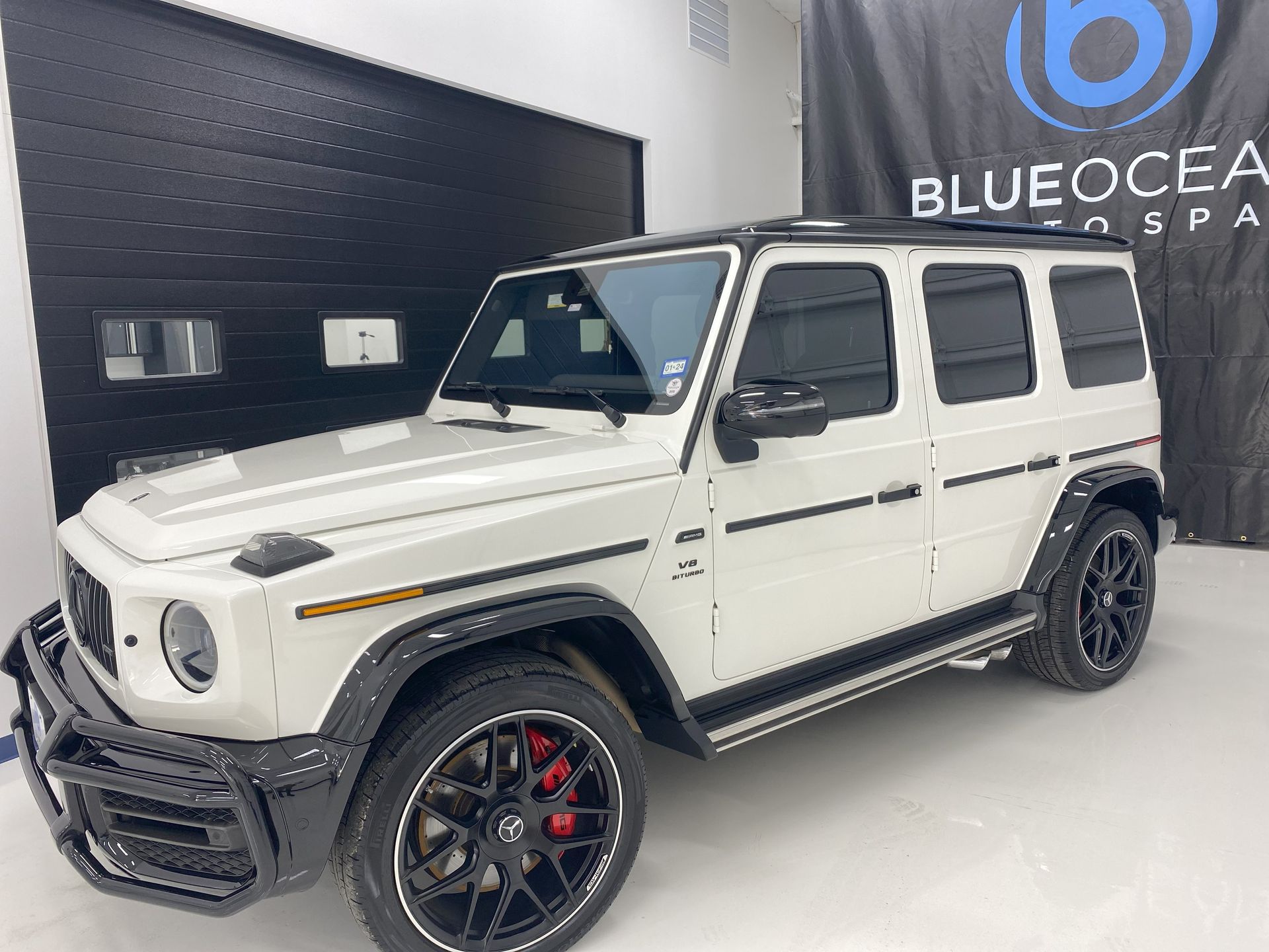 A white mercedes benz g63 amg is parked in a showroom.