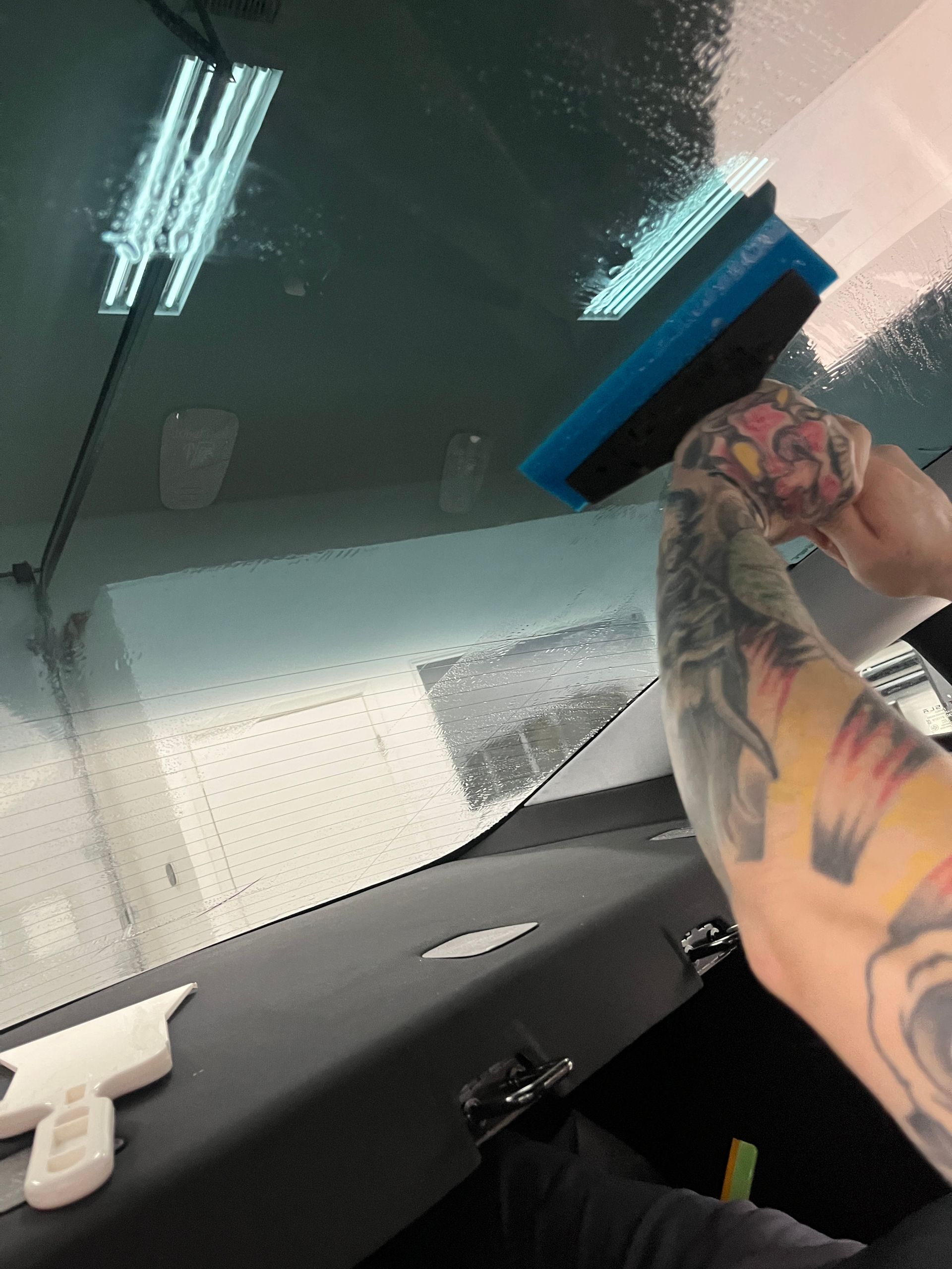 Blue Ocean Auto Spa of Cedar Park Tx technician shown using an 8 inch BlueMax squeegee to extract the slip solution during the installation of ceramic window tint to the oversized and high-difficulty level rear windshield of a Tesla Model 3.