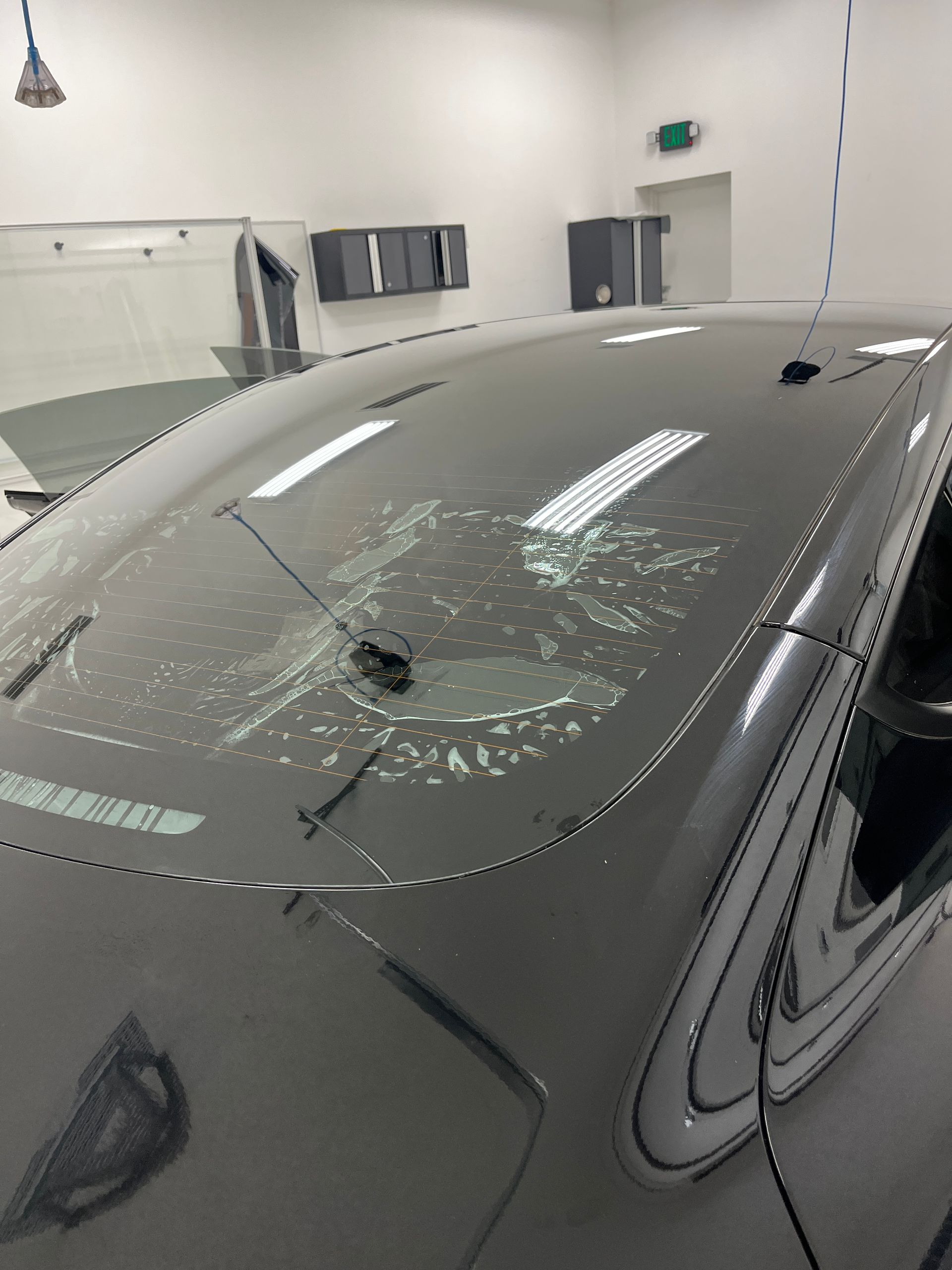 Exterior view of a Blue Ocean Auto Spa of Cedar Park Tx technician using an 8 inch BlueMax squeegee to extract the slip solution during the installation of ceramic window tint to the oversized and high-difficulty level rear windshield of a Tesla Model 3.