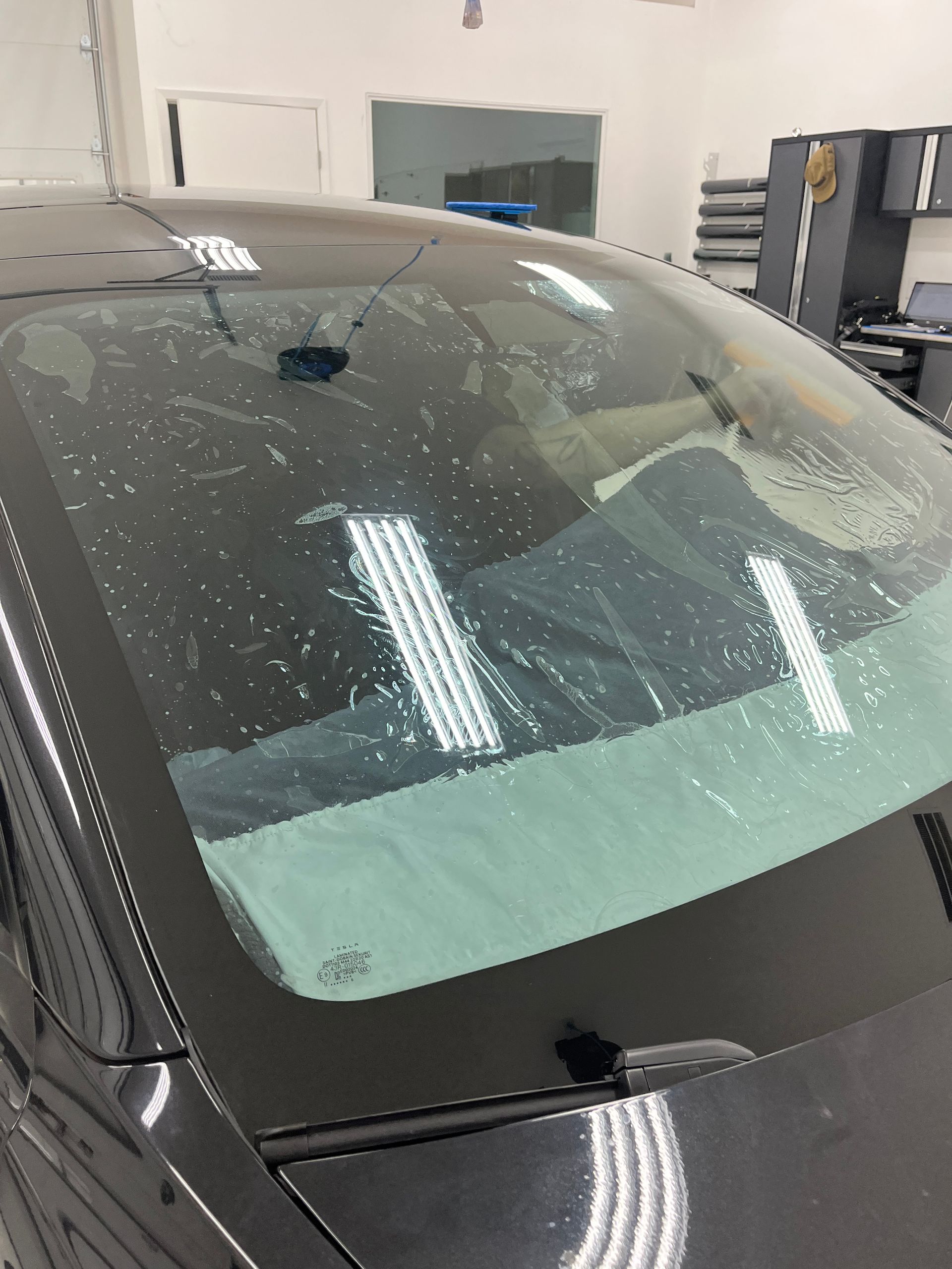A Blue Ocean Auto Spa Window Tint technician rolls out and position ceramic window tint on the front windshield of this Tesla Model 3.  He is using a water-proof dash cover to protect sensitive electronics from water damage.