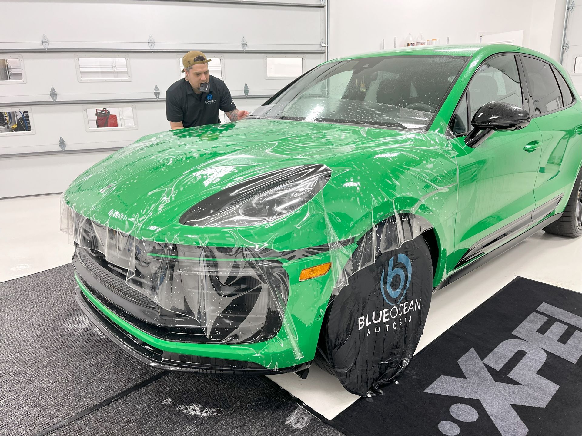 A man is covering a green car with plastic wrap.