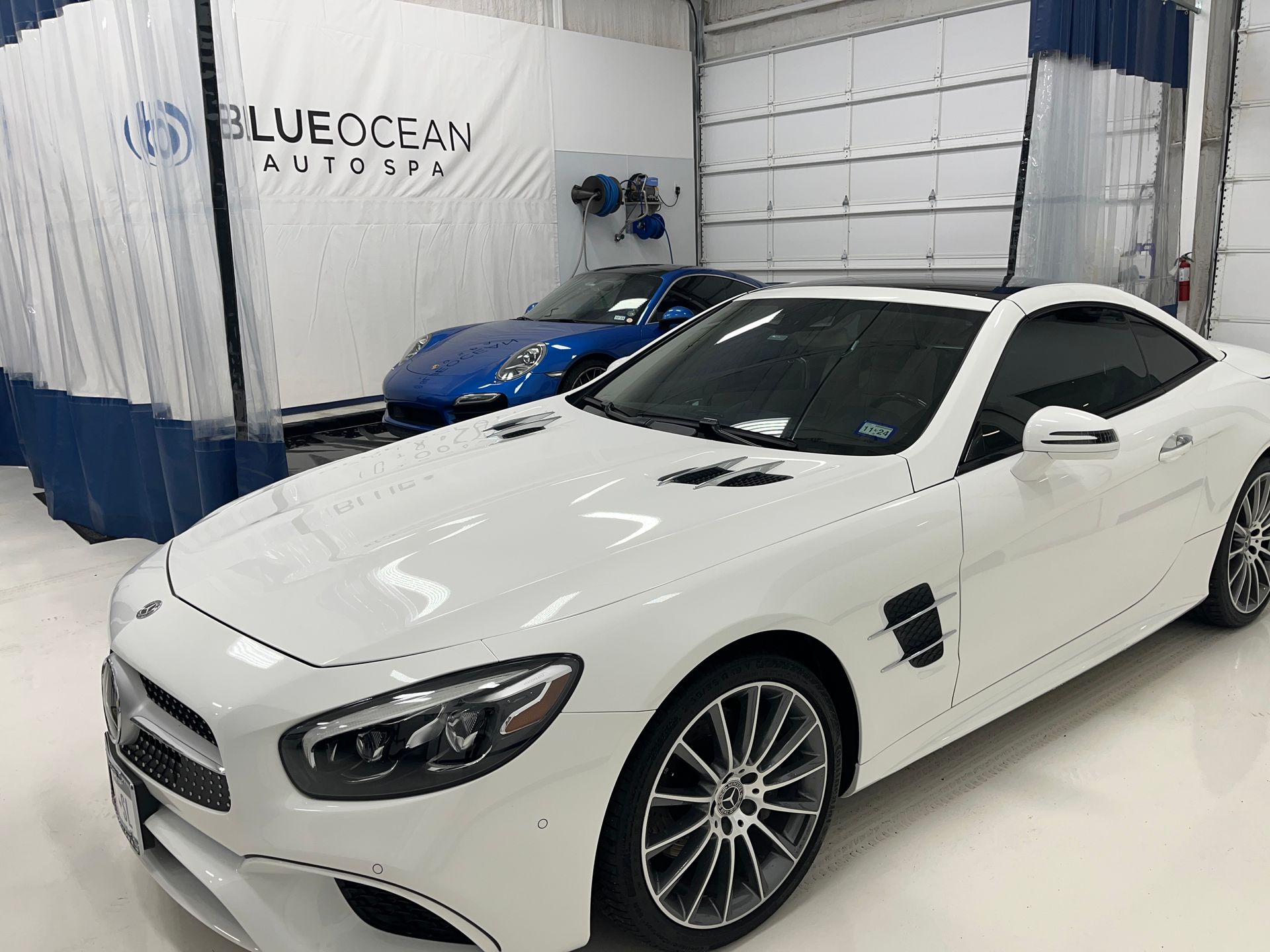 A white sports car is parked in a garage next to a blue sports car.
