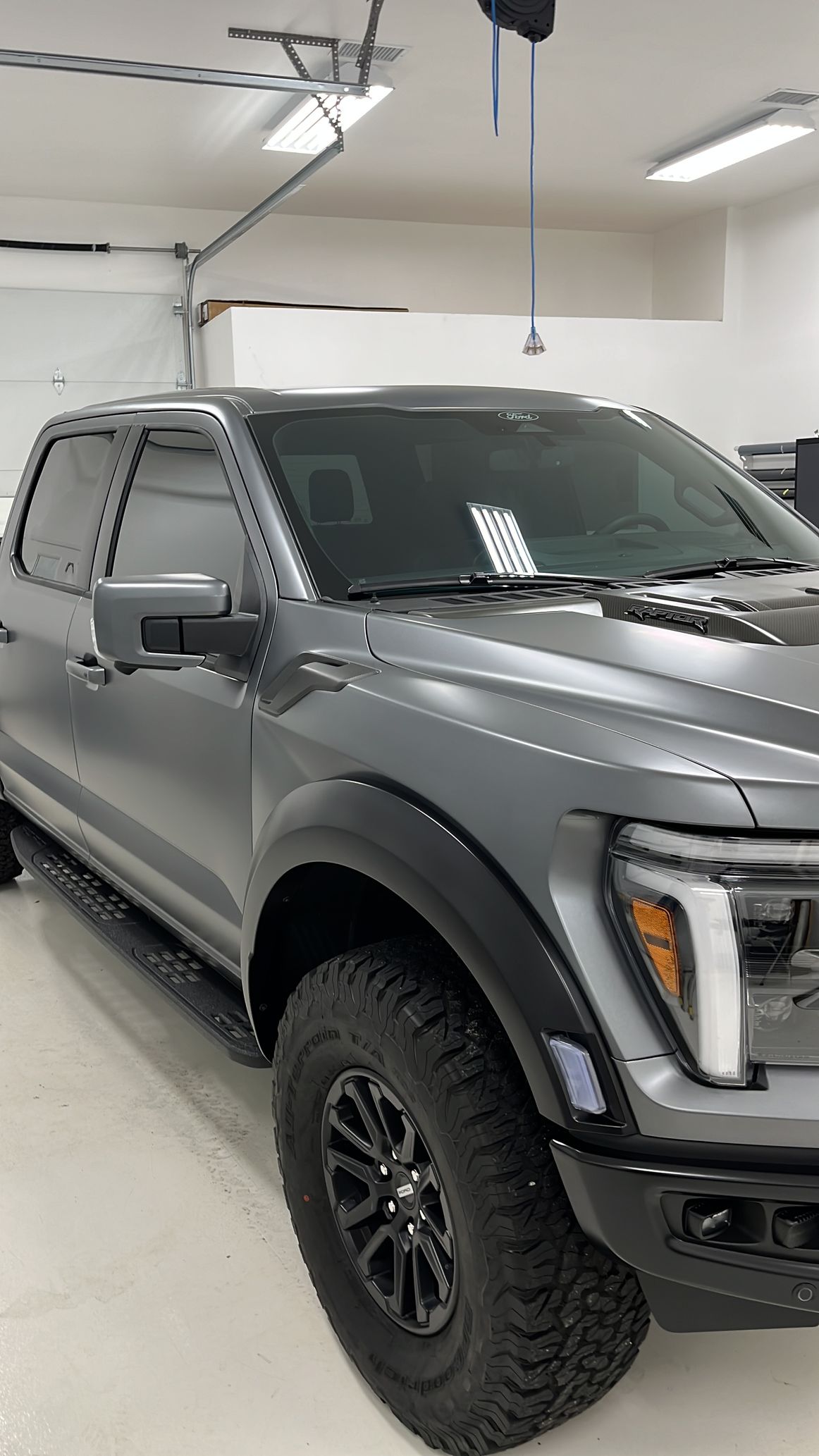 Gray Ford F-150 Raptor truck parked inside a garage. Black tires and fender flares are visible.