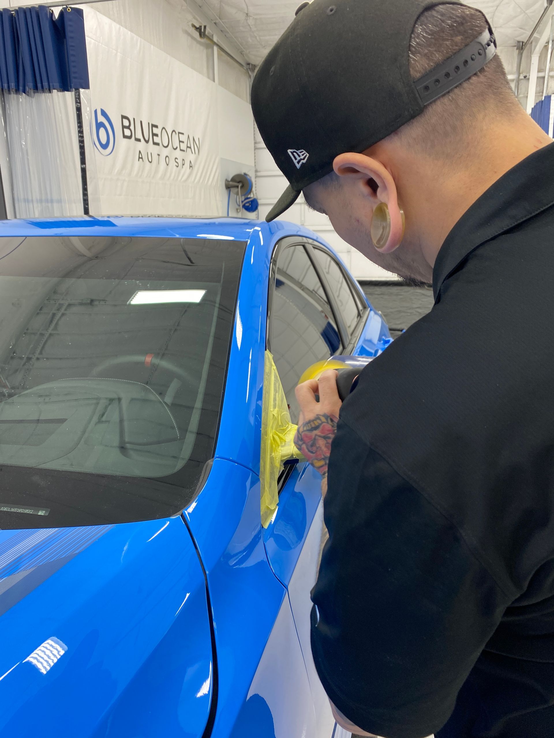 A man in a black hat is working on a blue car