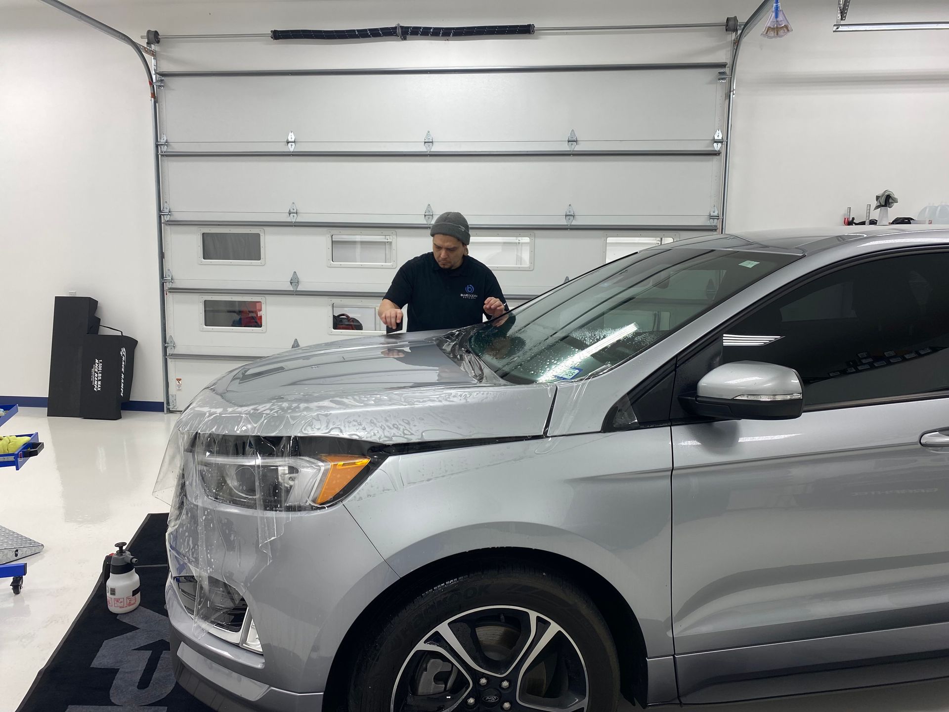 A man is wrapping a silver car in plastic in a garage.