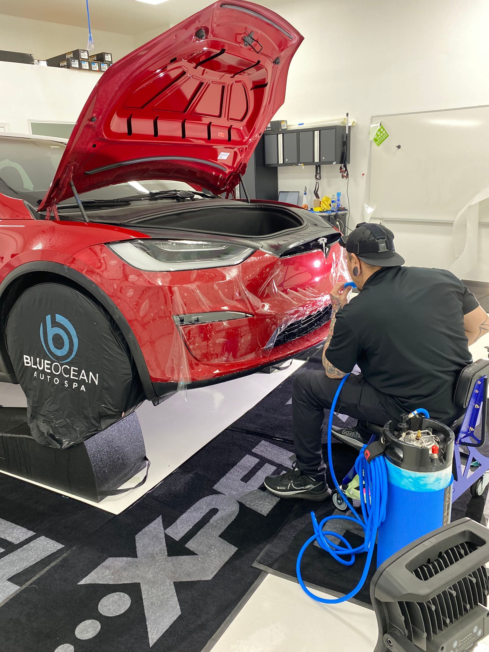 Two men are working on a red tesla model x in a garage.