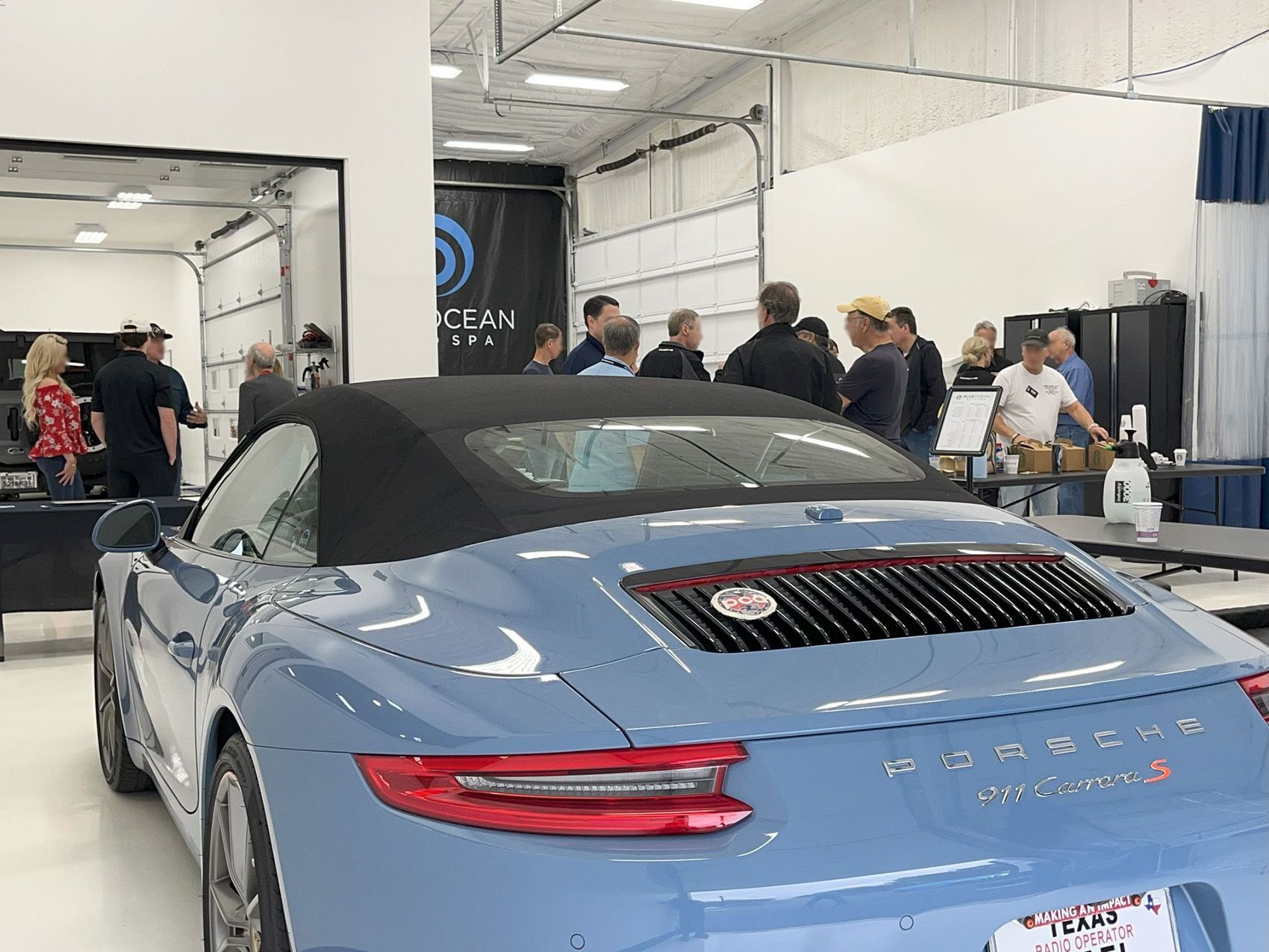 A group of people are standing around a blue porsche convertible in a garage.