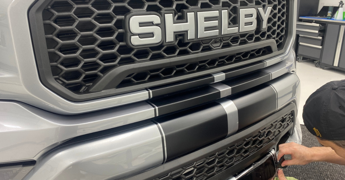 A man is wrapping the front bumper of a shelby truck.