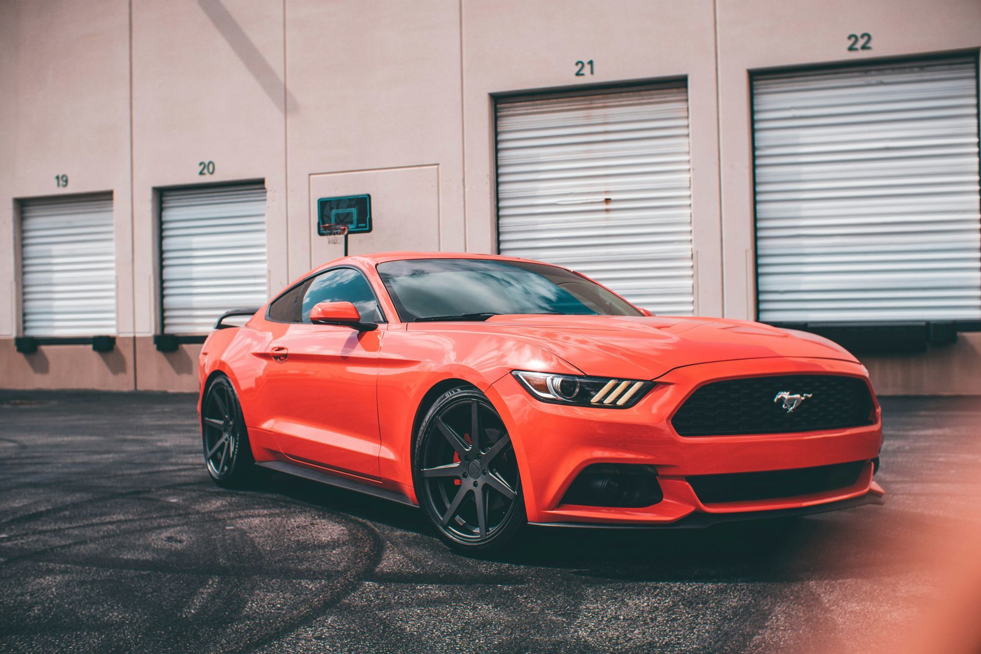 A red mustang is parked in front of a building.