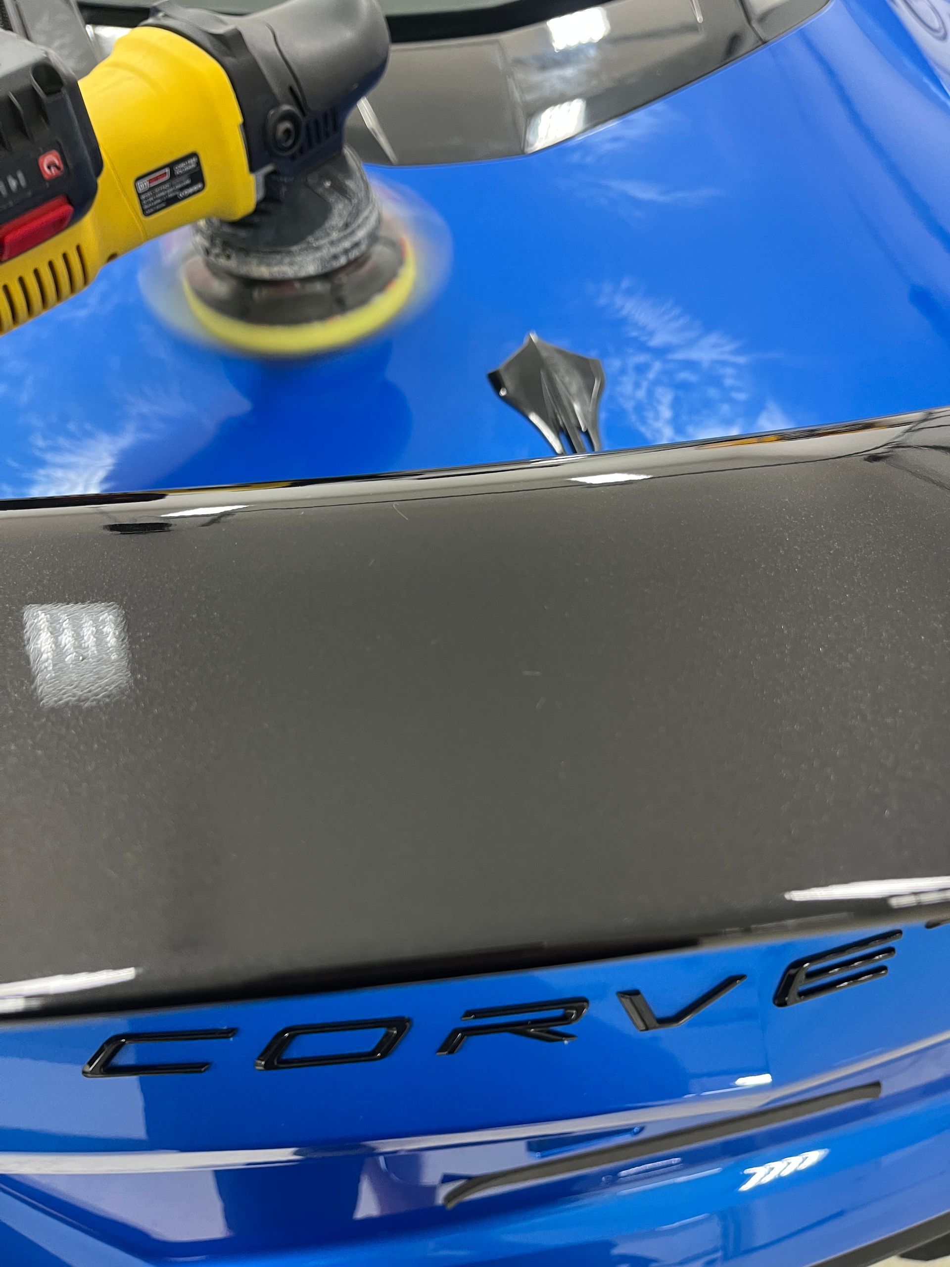 Machine polisher working on blue C7 Corvette paint under professional shop lighting