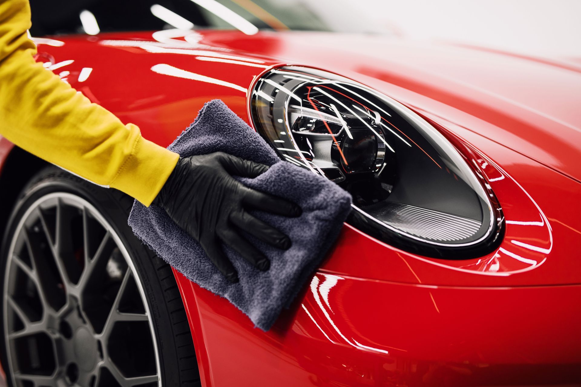 A person is cleaning a red car with a towel.
