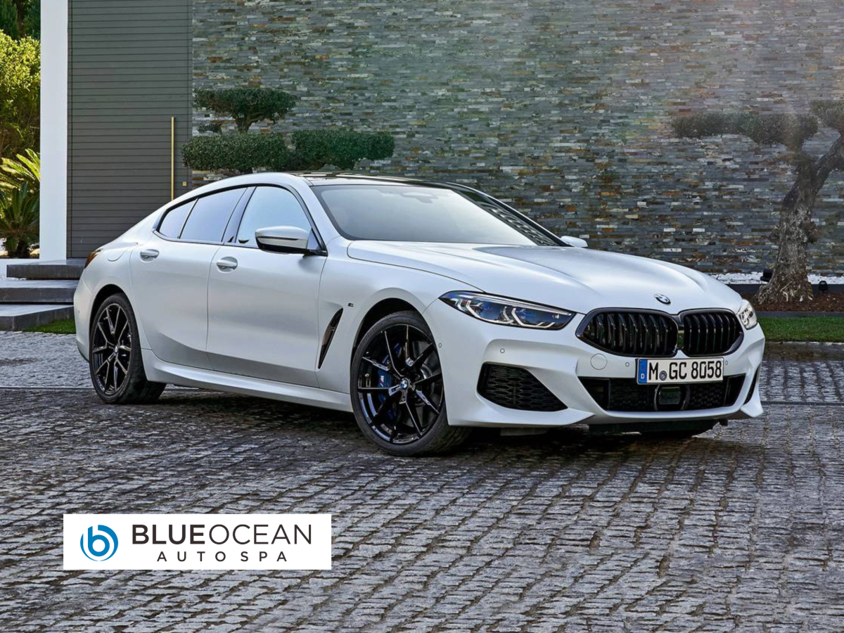 A white bmw 8 series is parked on a cobblestone driveway in front of a house.