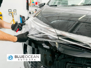 A man is wrapping a black car with plastic wrap.