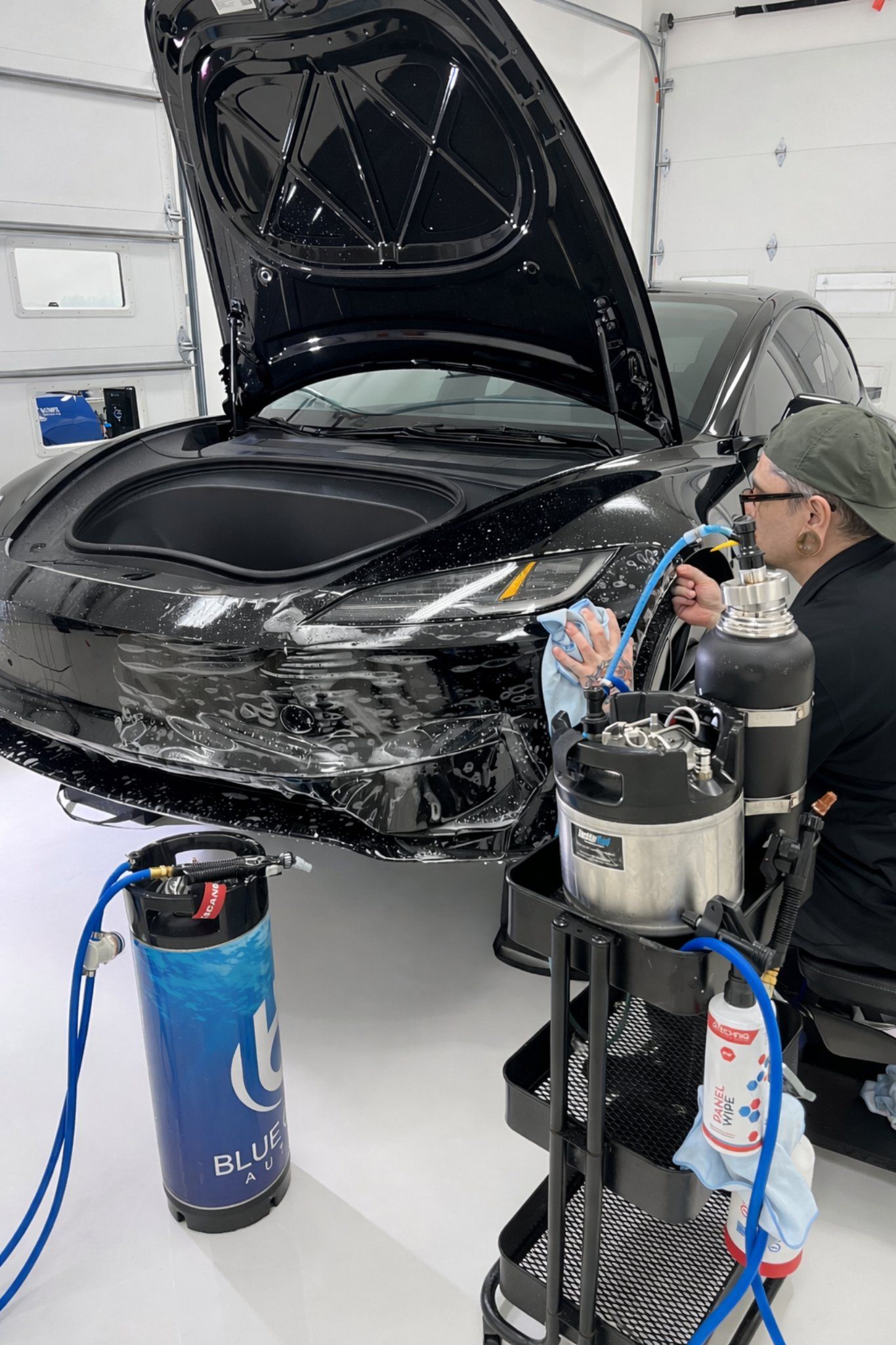 Our technician sprays slip solution on the front bumper of a Tesla Model Y as they align the paint protection film before locking down the PPF.