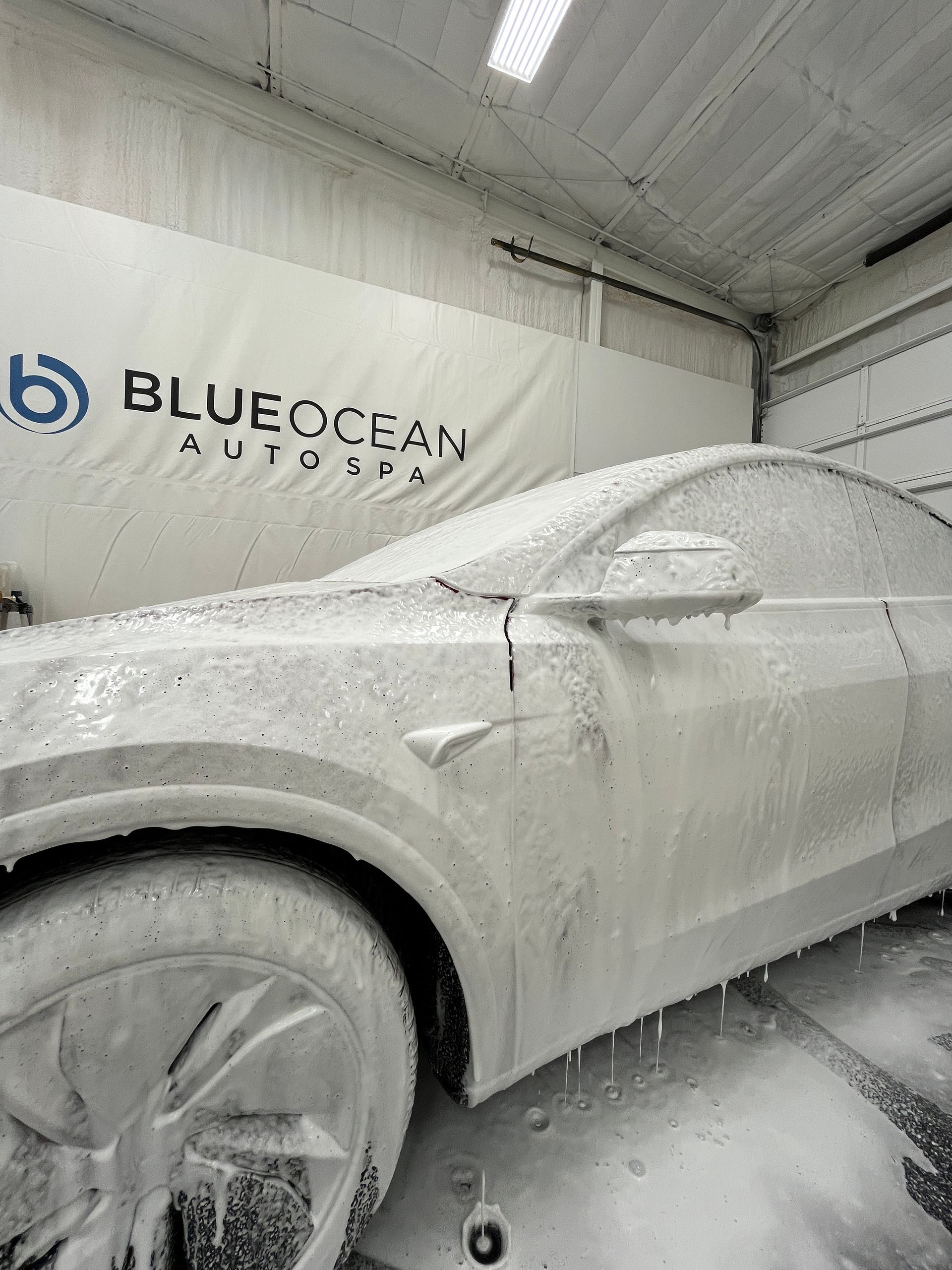 Installer uses a heat gun on window tint film applied to a car door, helping the material conform smoothly to the glass surface. The tint darkens the window while reflections of the workspace remain visible.