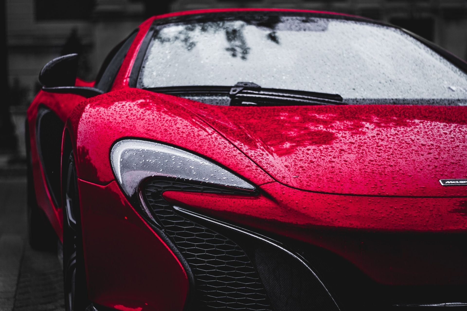 A red sports car is parked on the side of the road in the rain.