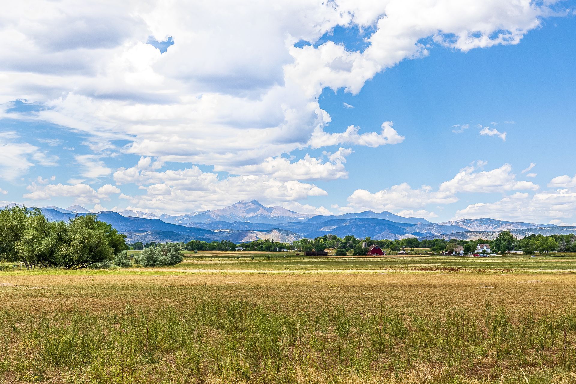 A field with mountains in the background and a blue sky with clouds