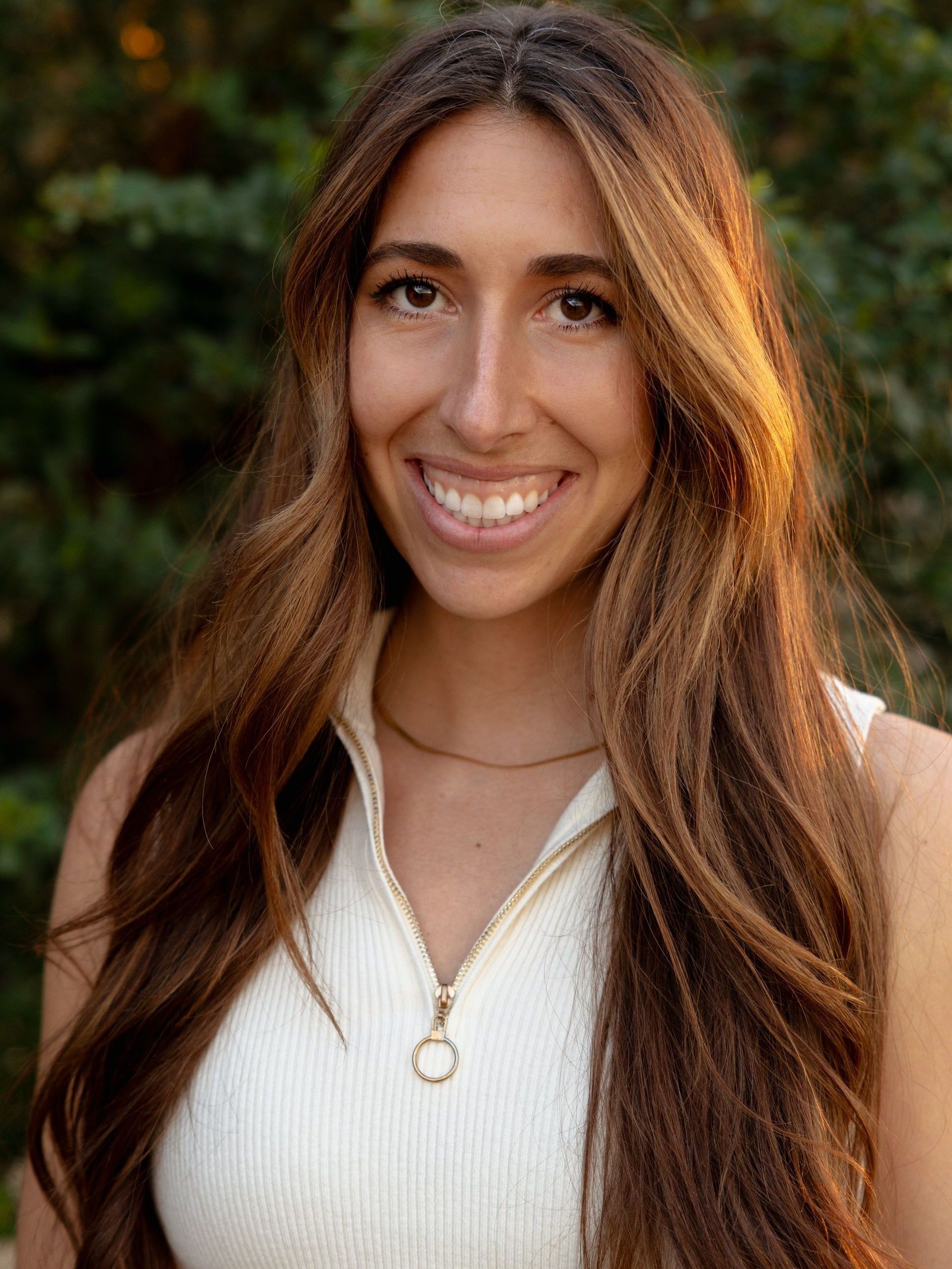 A woman in a white shirt is sitting on a couch and smiling.