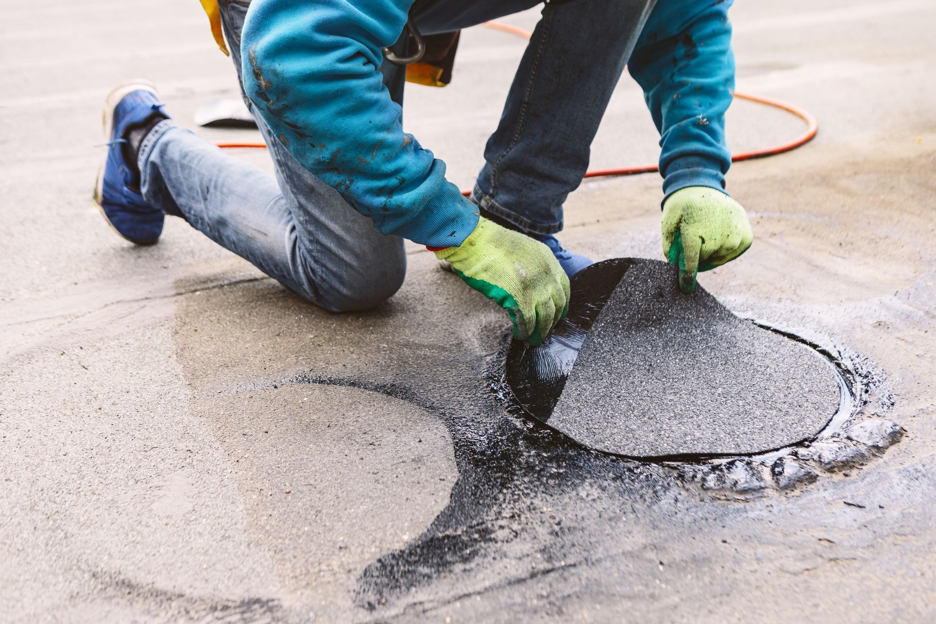 Worker kneeling to patch cracked pavement with asphalt on a road surface
