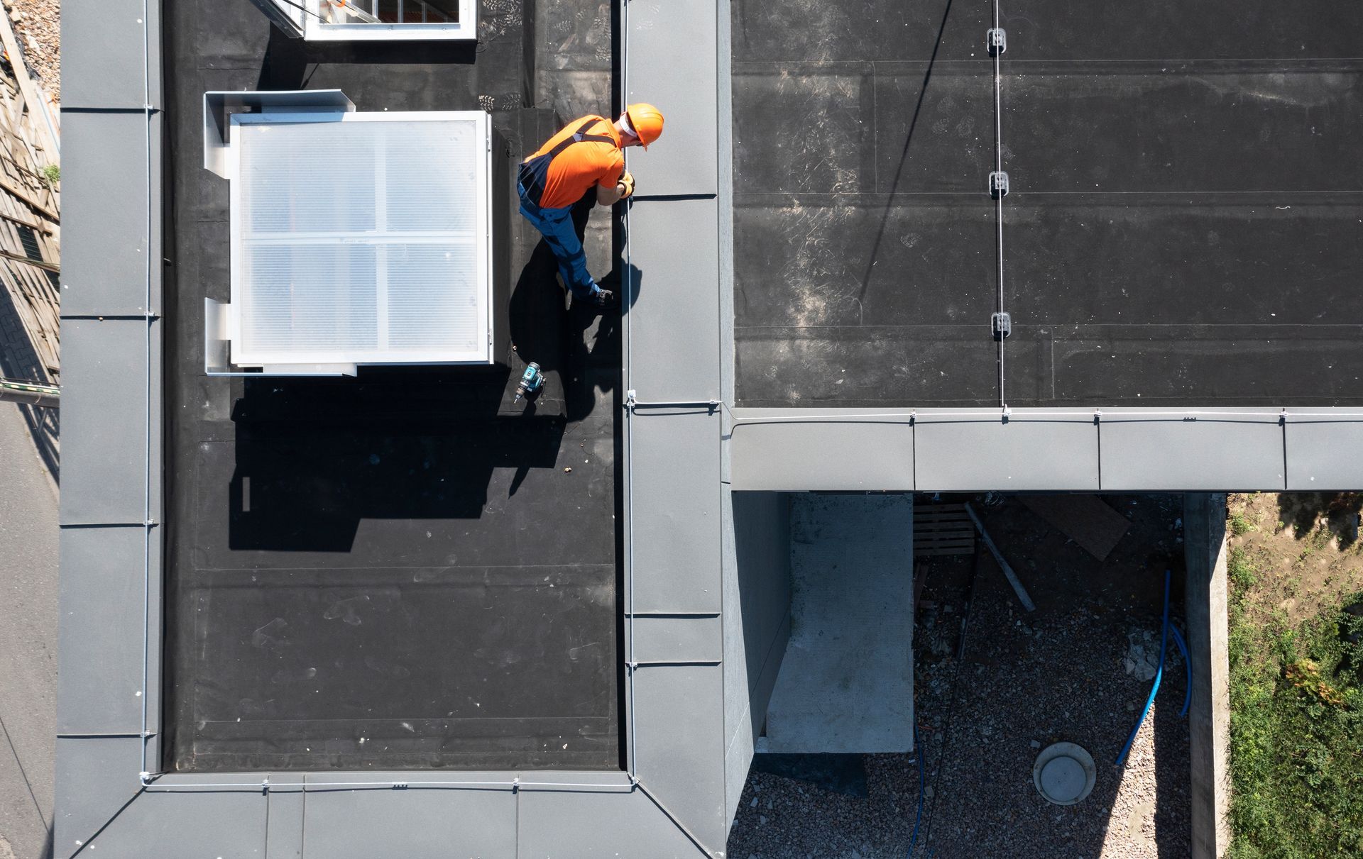 Person in an orange shirt working on a flat roof beside a white skylight.
