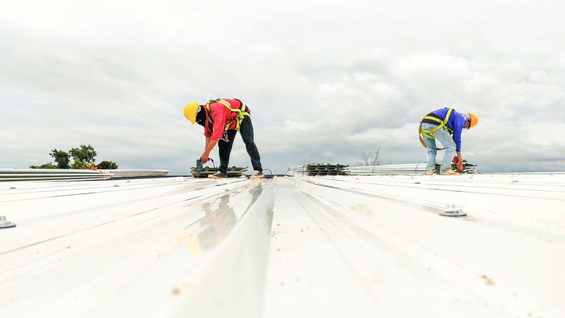 Two workers in hard hats kneel on a white rooftop under a cloudy sky, installing panels.