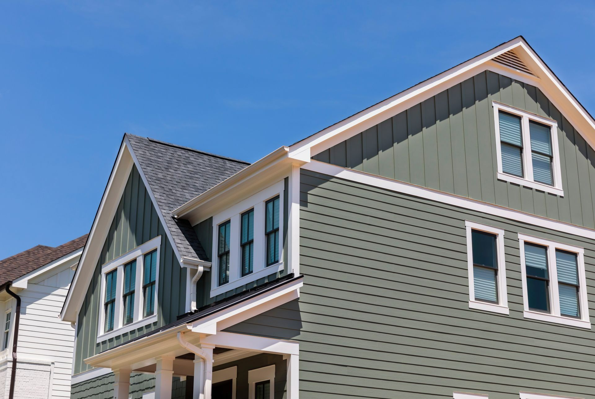Green-sided house with white trim and dark roof against a blue sky