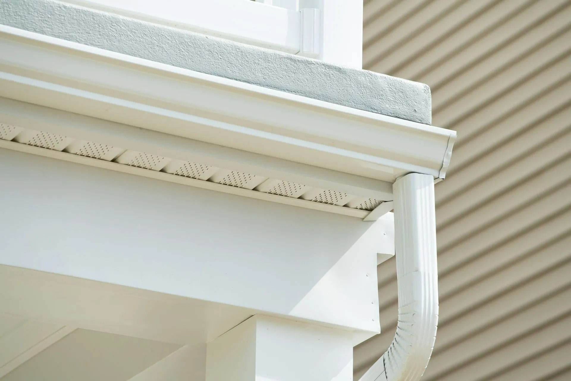 White house eave and gutter with downspout against a bright exterior wall