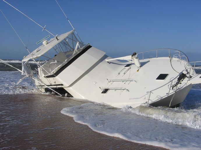Stranded white boat tilted on a beach as waves wash around it under a clear blue sky
