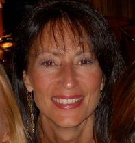 Smiling woman with dark hair and red lipstick in a dimly lit indoor setting