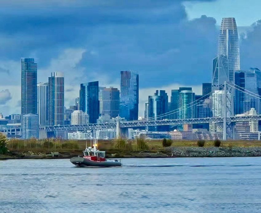 City skyline across a river with a small boat in the foreground and a blue sky