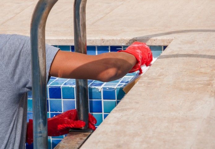 Worker cleaning pool tiles with red gloves beside a metal ladder