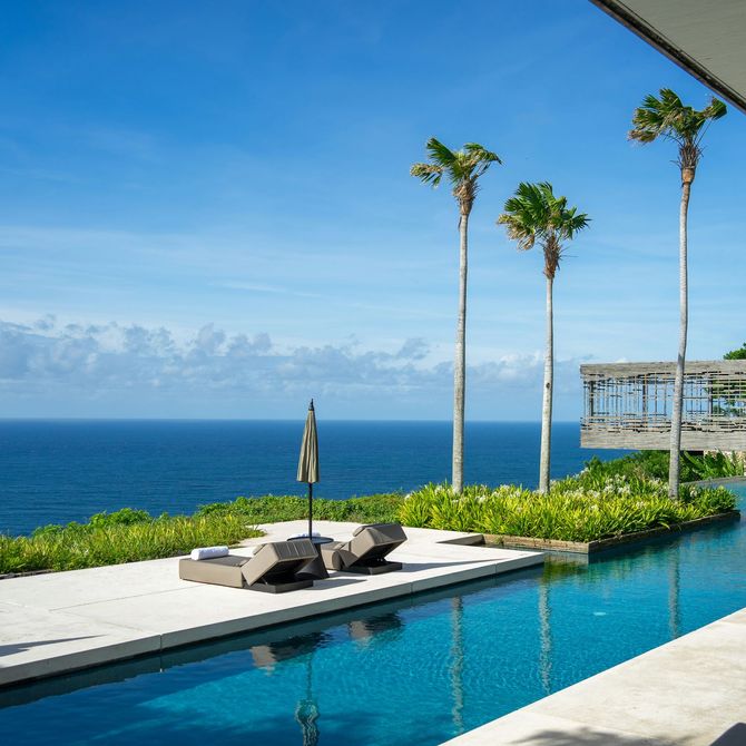 Luxury oceanfront infinity pool with lounge chairs, palm trees, and blue sea under a clear sky