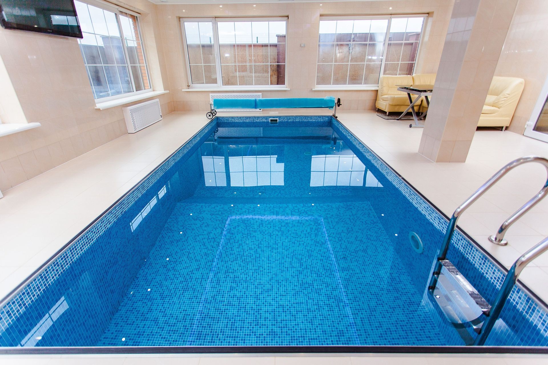 Indoor swimming pool with blue water, metal handrail, and lounge chairs by large windows