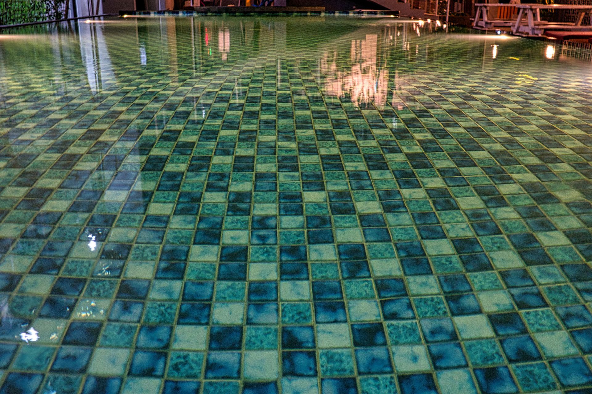 Green-blue tiled pool or plaza surface with reflections of lights at night