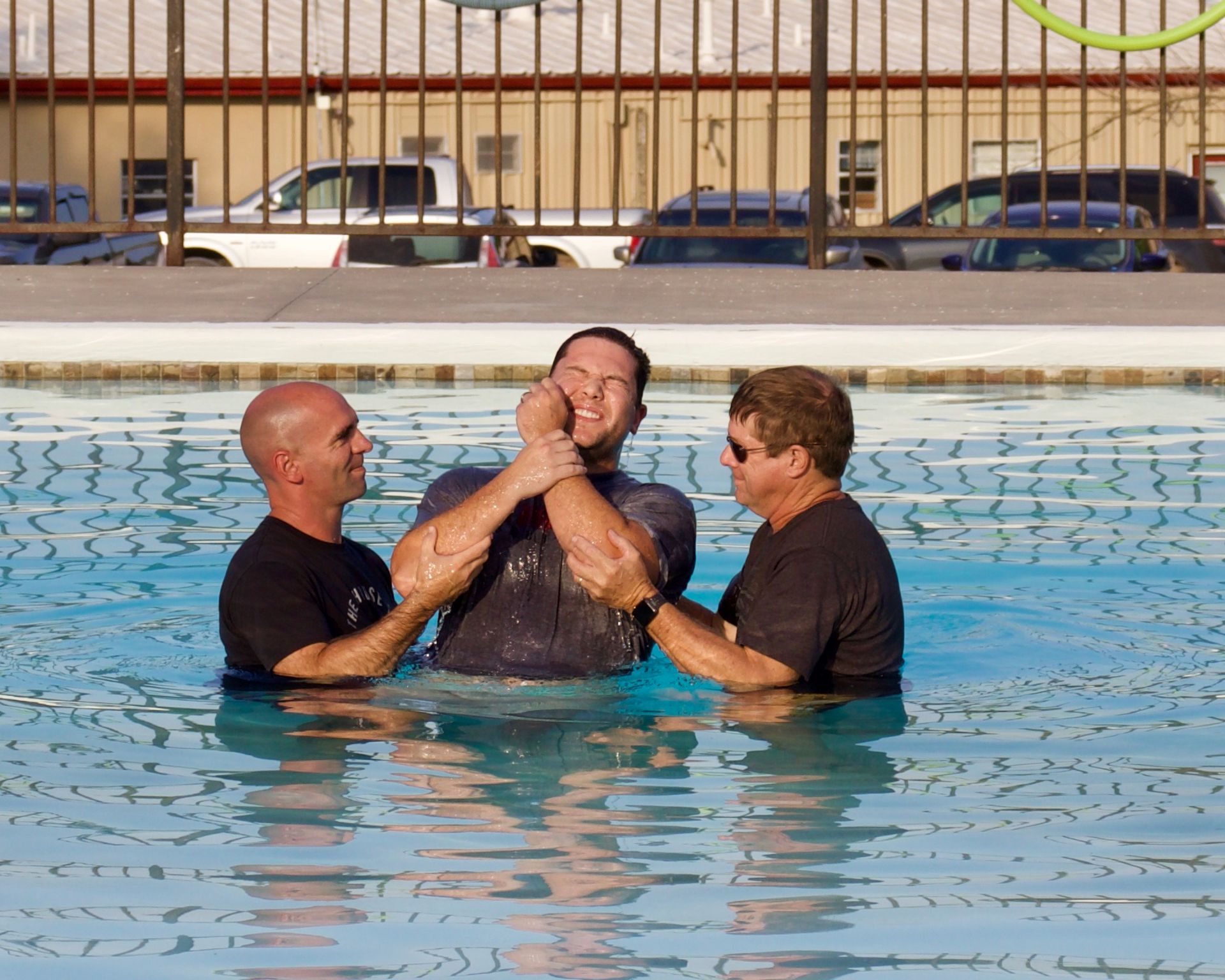 Two men are baptizing a man in a swimming pool