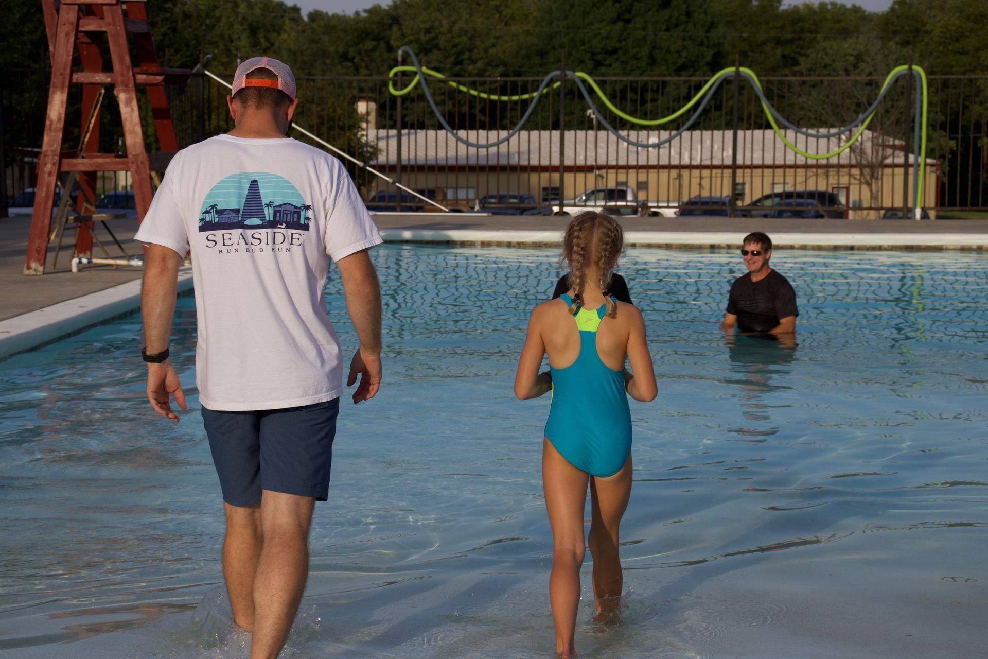 A man and a girl are walking into a swimming pool.