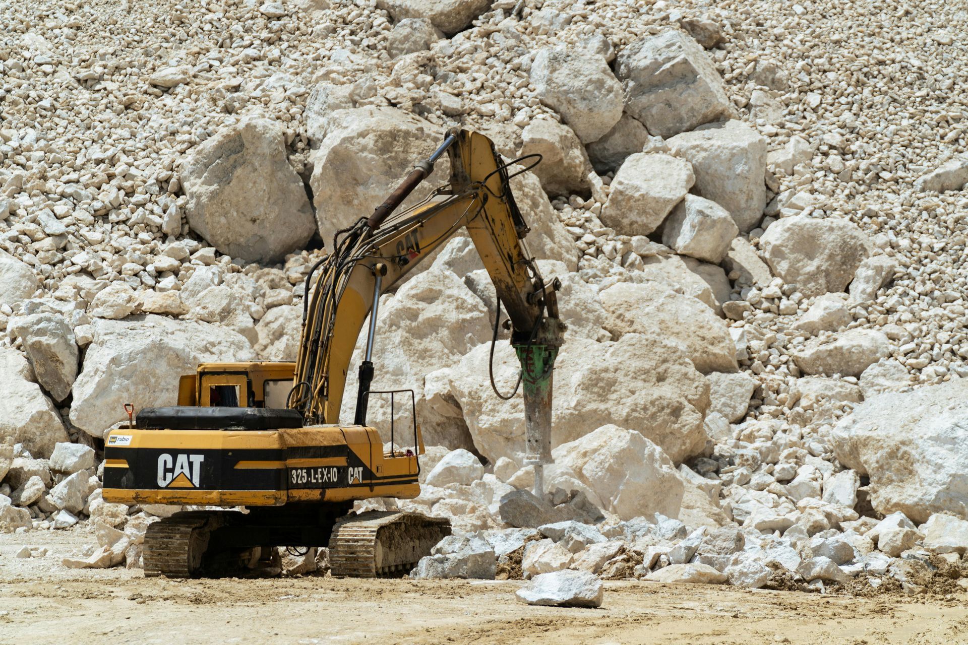 Gray machine dispensing a large pile of dark material onto a paved area; possible soil or aggregate.