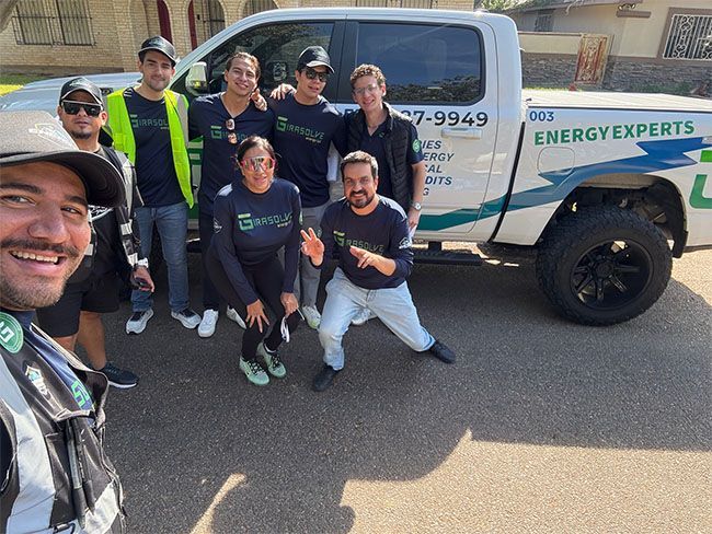 Group of six smiling people posing beside a white ENERGY EXPERTS truck outdoors
