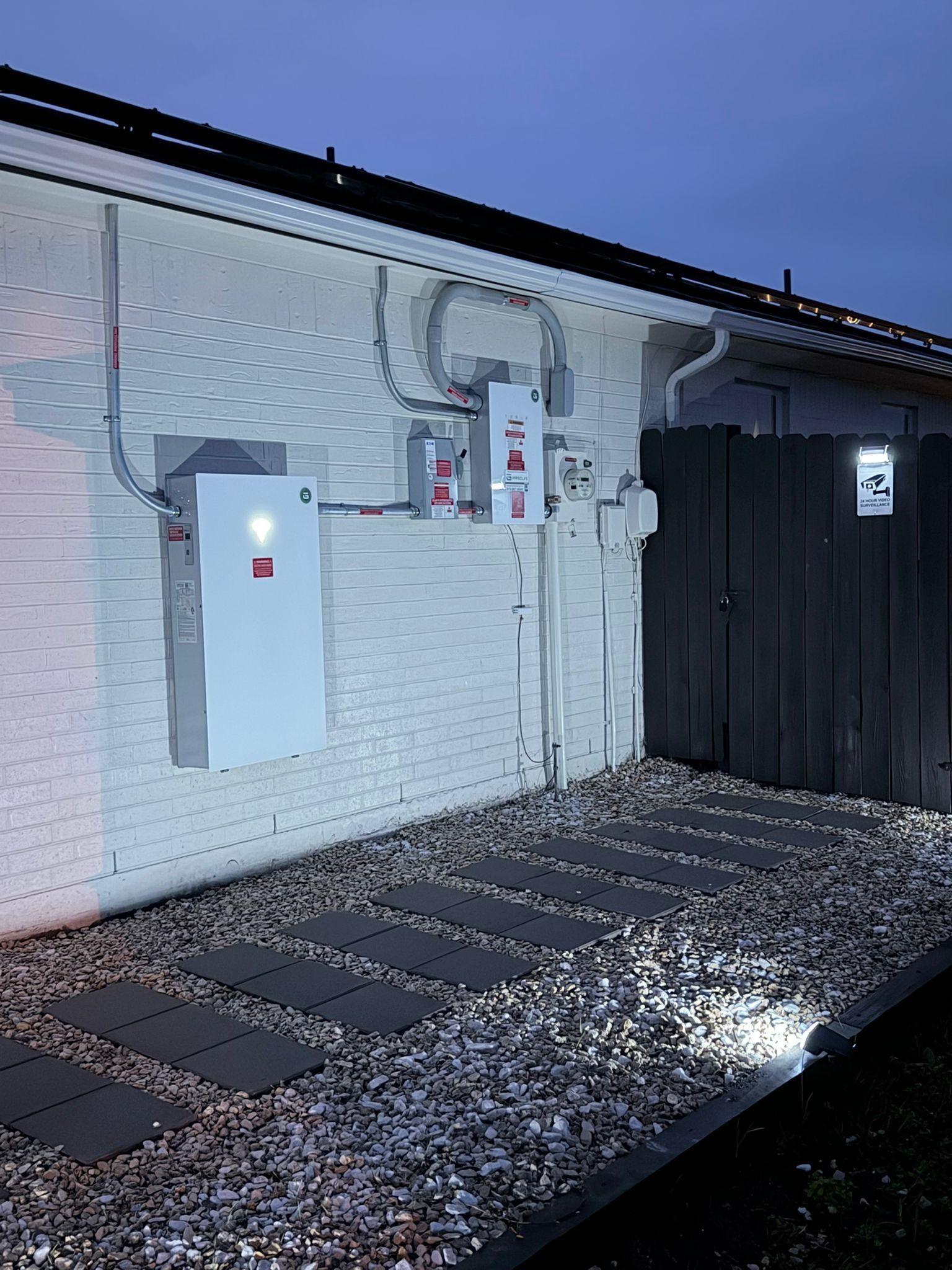 Outdoor utility area beside a white brick building with electrical boxes and dark metal siding at night