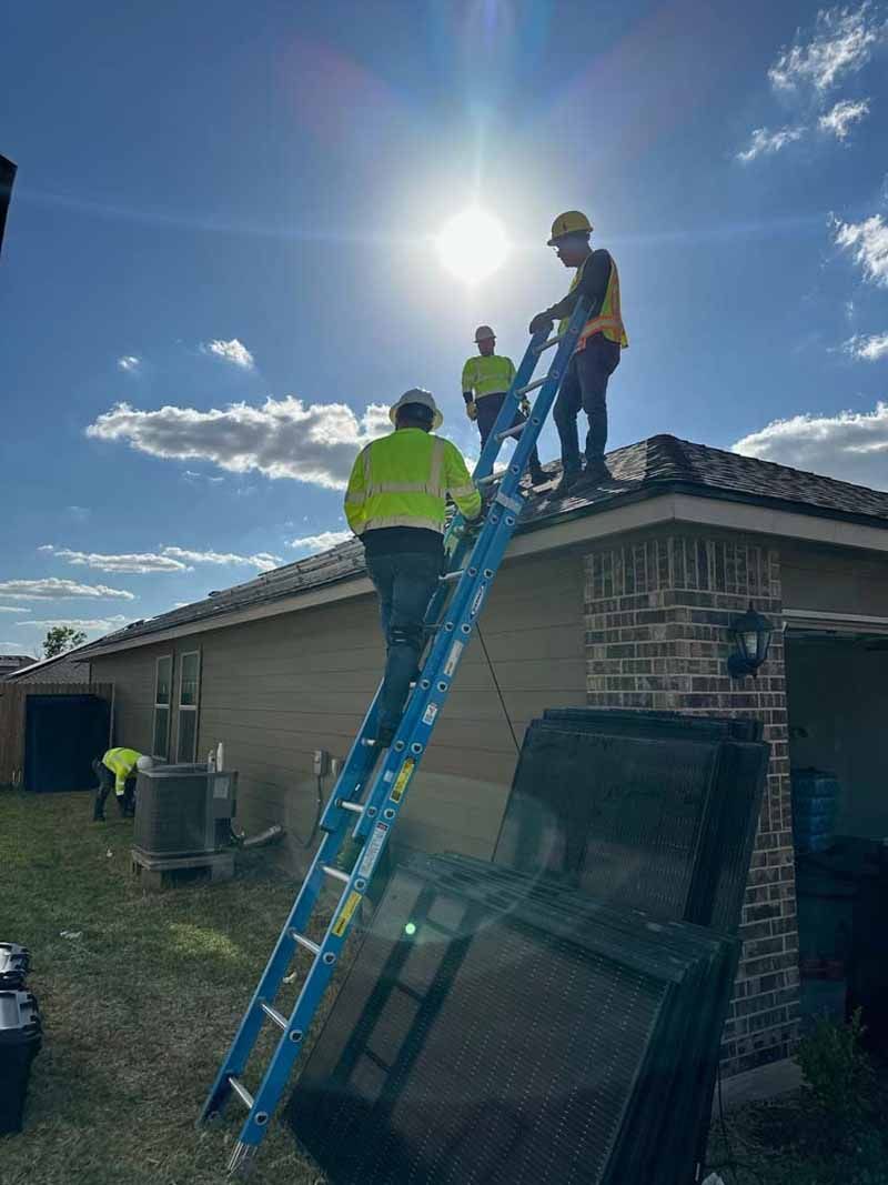 Workers on a roof installing solar panels beside a blue ladder under a bright sun.