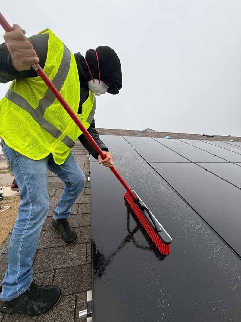 Worker in a neon safety vest cleaning a rooftop with a long-handled brush.