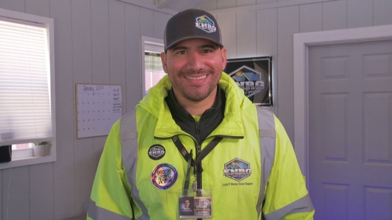 Smiling worker in neon safety jacket and cap standing indoors near doors and windows