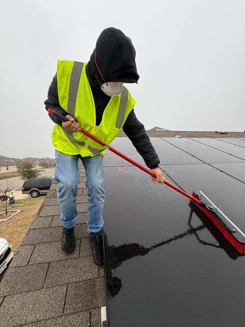 Worker in neon vest scraping snow from a rooftop with a long red tool