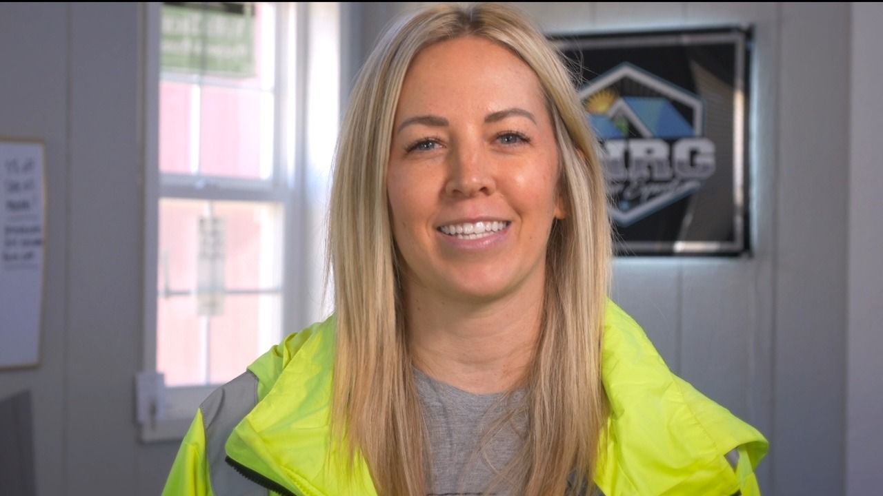 Smiling blonde woman in a neon yellow jacket standing indoors
