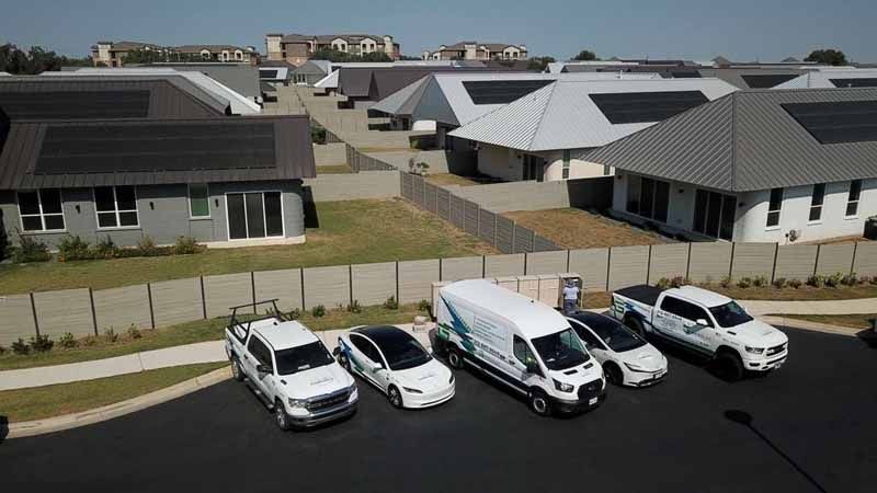 Four white work vehicles parked in front of modern houses on a sunny suburban street.