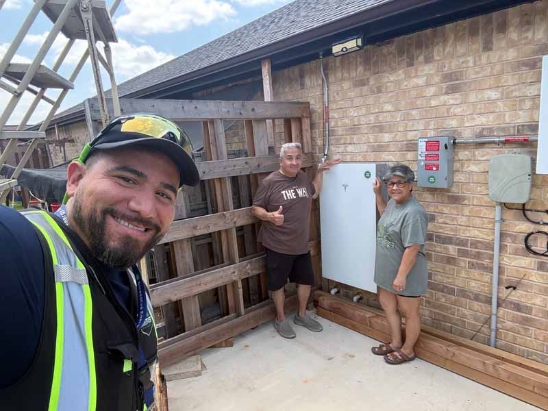 Selfie at a rooftop utility area with two people by a white cabinet and electrical boxes on a brick wall.